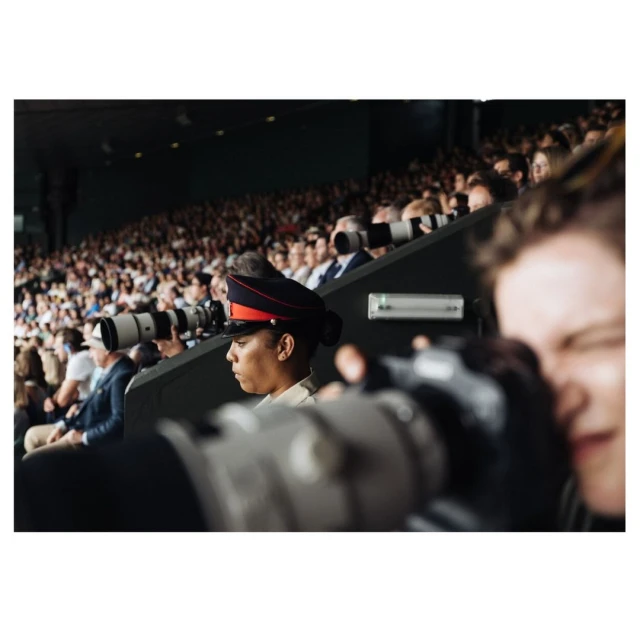 Crowd scene at a stadium with a military guard in dress uniform and photographers with long lenses capturing the event.
