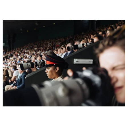 Crowd scene at a stadium with a military guard in dress uniform and photographers with long lenses capturing the event.