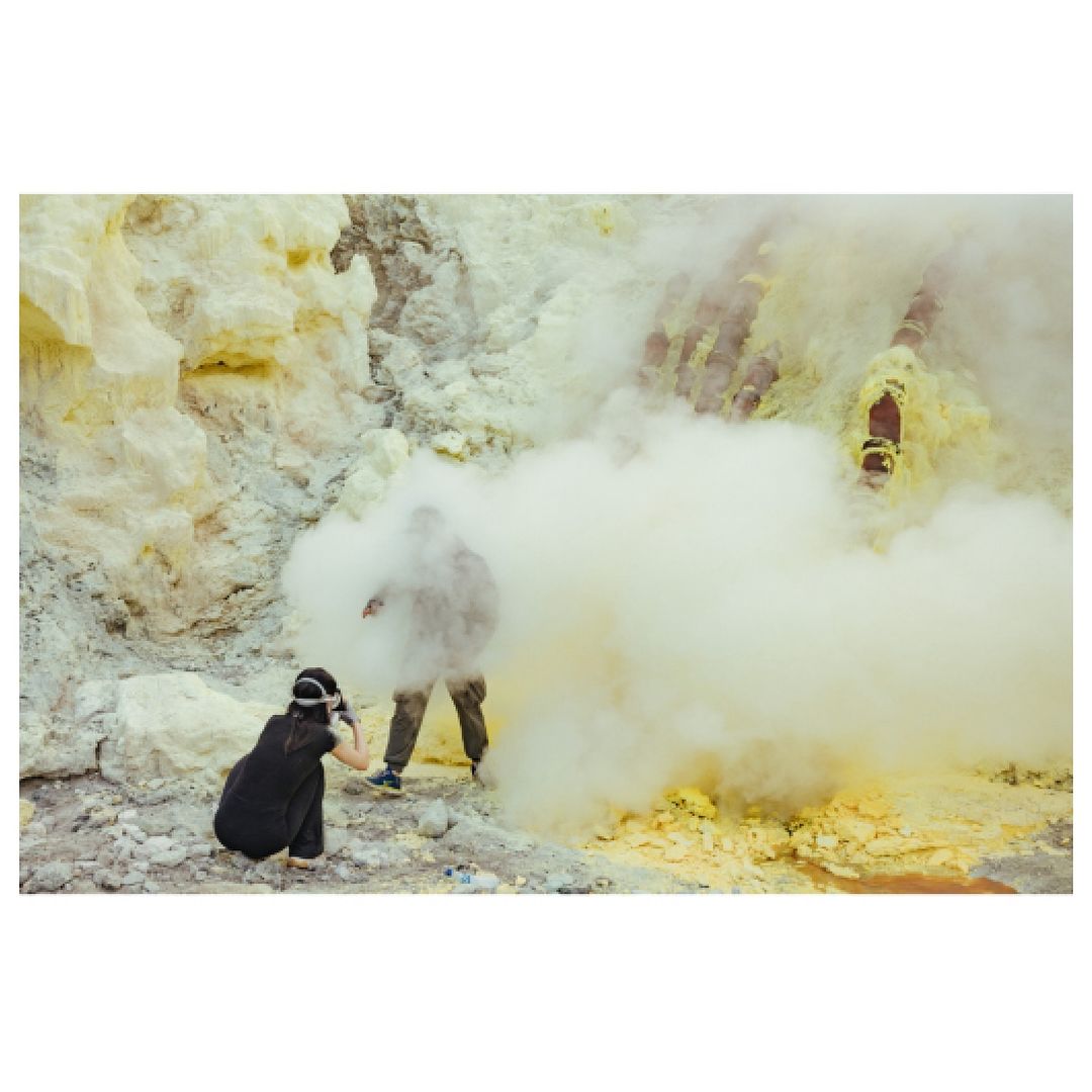Photographer capturing an adult human in a misty, rocky landscape with yellowish hues, highlighting nature and travel photography.