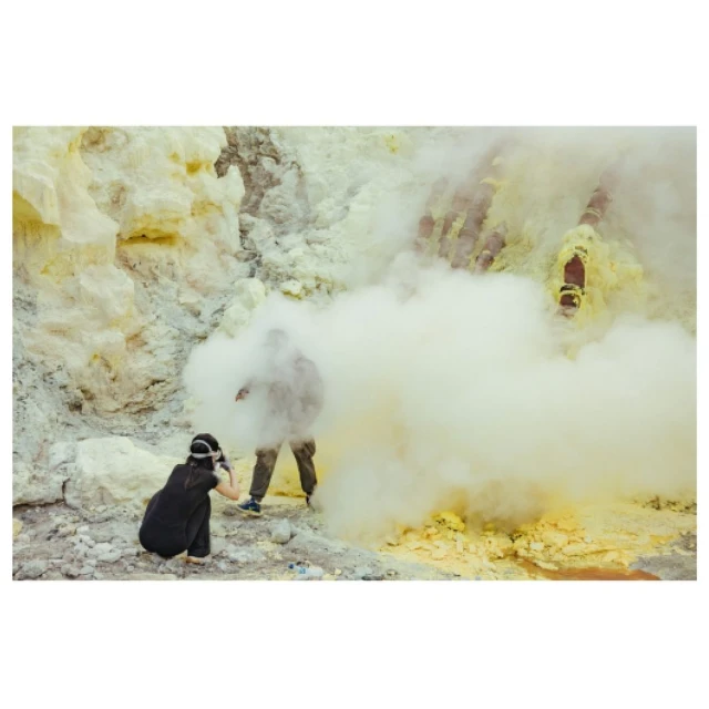 Photographer capturing an adult human in a misty, rocky landscape with yellowish hues, highlighting nature and travel photography.