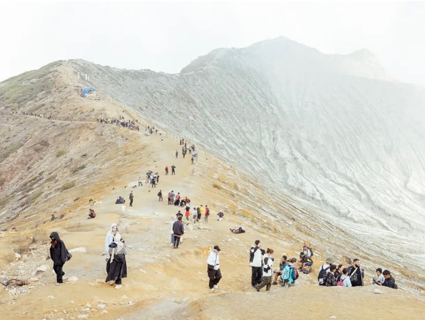 Landscape with a large group of people on a ridge and volcanic mountain with white and grey textured rock and trail in daylight.