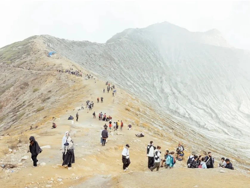 Landscape with a large group of people on a ridge and volcanic mountain with white and grey textured rock and trail in daylight.