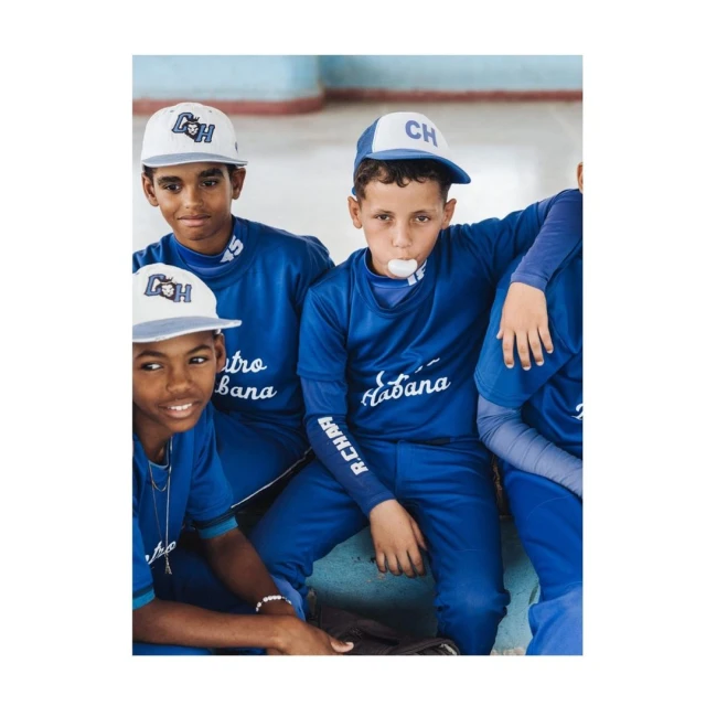 Group of young baseball players in matching blue uniforms and caps gather indoors, one blowing bubblegum, showcasing youth sports.