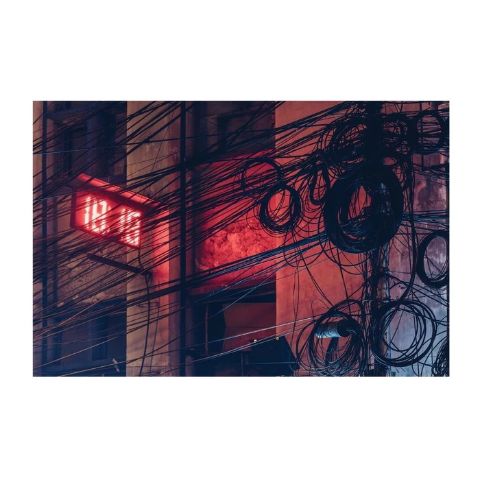 Dense tangle of dark overhead cables and coiled wires against a red-lit building exterior in London.