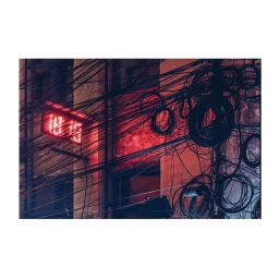 Dense tangle of dark overhead cables and coiled wires against a red-lit building exterior in London.