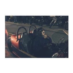 A man wearing a cap sitting inside a red three-wheeled Morgan sports car at night, captured by Tom Parker.