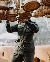 Man in green military-style uniform reaching up towards an arrangement of hanging lanterns