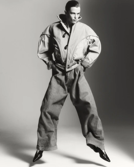 Black and white fashion shot of an adult woman with hands in pockets, wearing oversized jacket and pants, with a light grey background.
