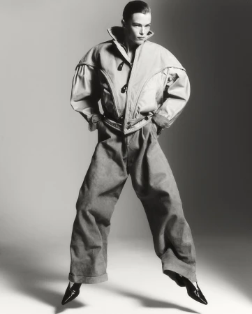 Black and white fashion shot of an adult woman with hands in pockets, wearing oversized jacket and pants, with a light grey background.