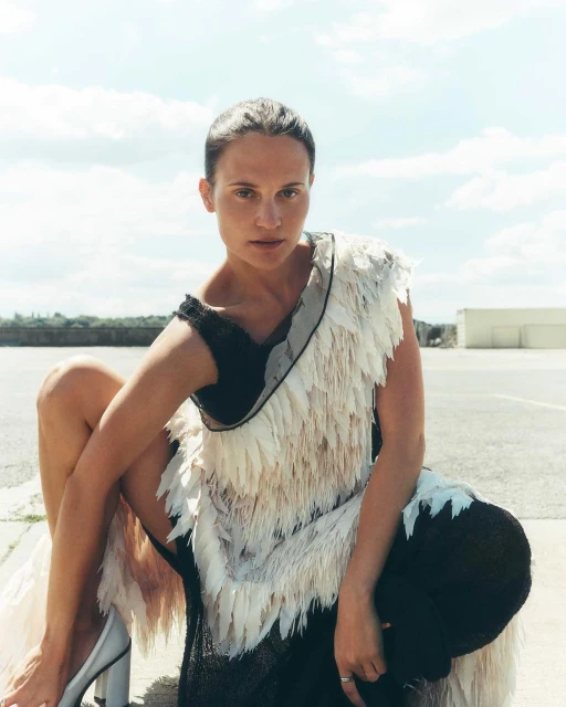 A model poses in a black and white textured dress outside against a sky backdrop. The fashion shoot captures an urban scene with natural light.