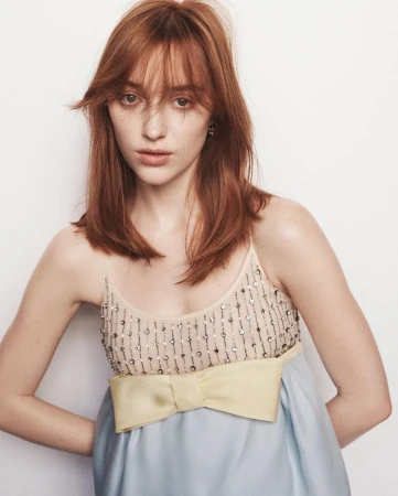 Red-haired female model wearing a pastel dress with a yellow bow detail against a white background.