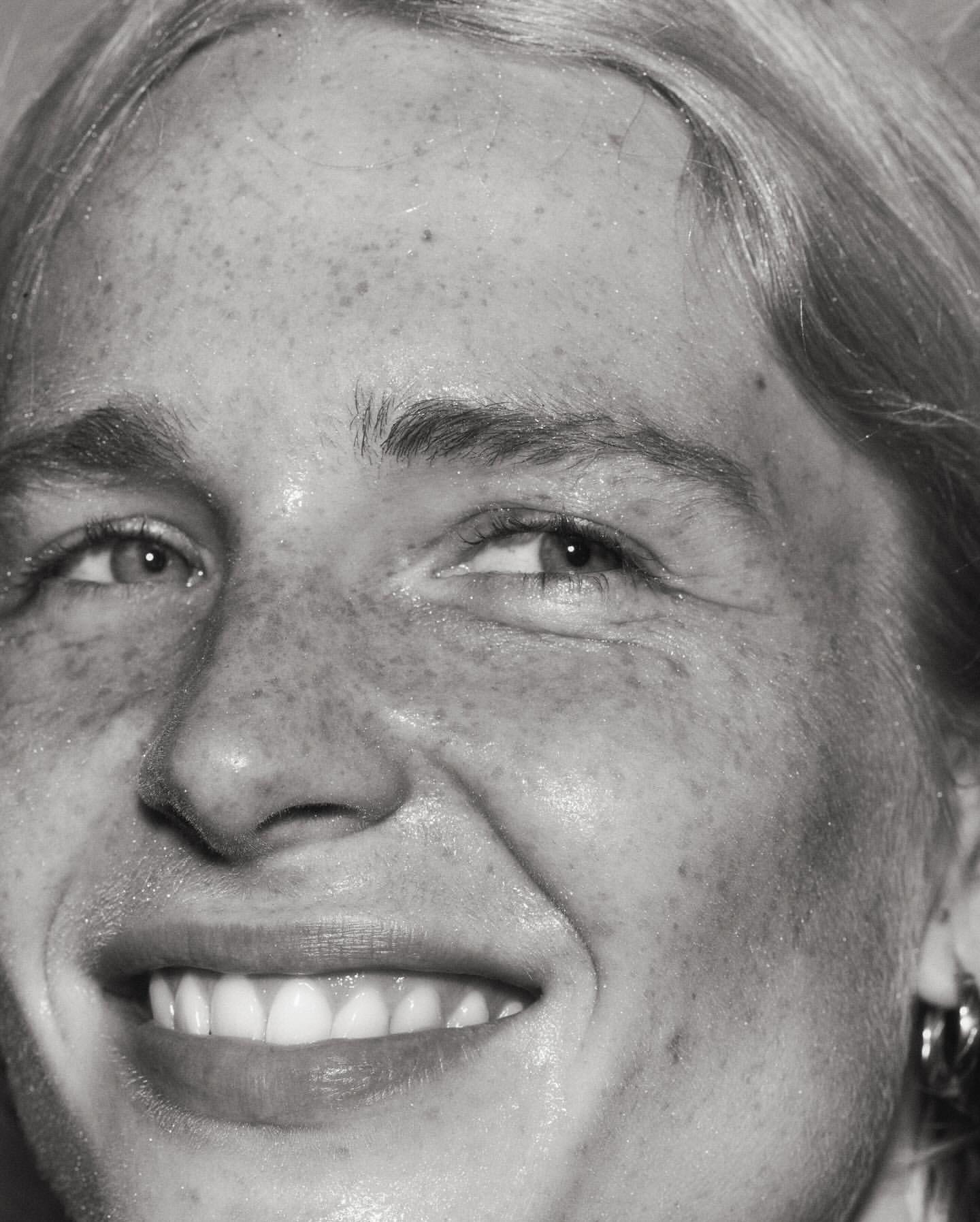 Close-up monochrome portrait of a smiling woman showing detailed facial features and visible skin texture.