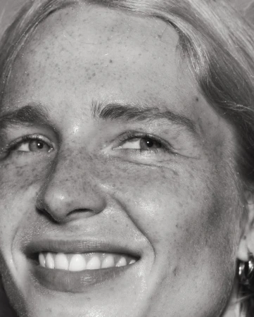 Close-up monochrome portrait of a smiling woman showing detailed facial features and visible skin texture.