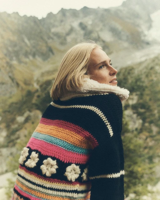 Woman in colorful knit sweater with mountainous landscape background, outdoors. Female fashion portrait in nature setting, back view.