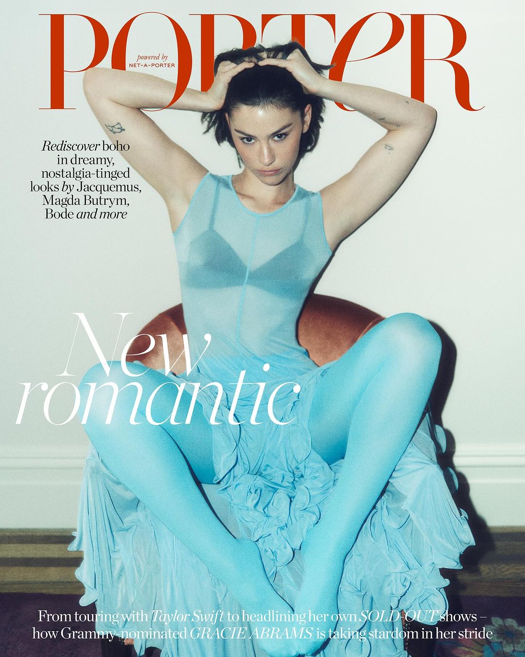 Gracie Abrams graces Porter cover in a dreamy blue dress, seated, with hands in her hair. 'New Romantic' text overlay, red Porter logo.