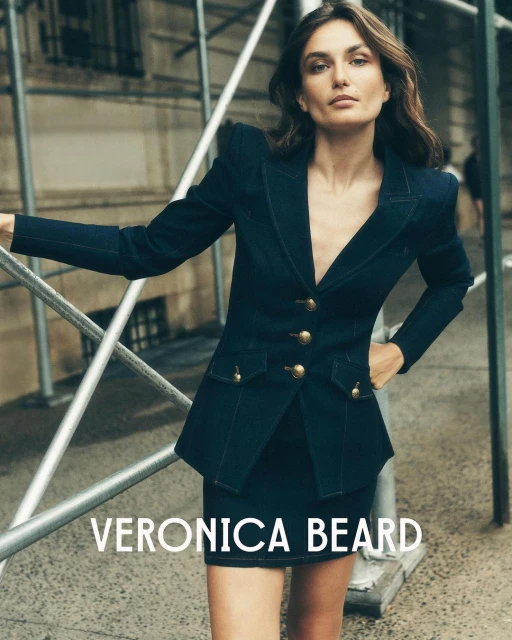 A woman wearing a navy Veronica Beard blazer and skirt poses outdoors in an urban setting; the clothing is the main focus of the image.