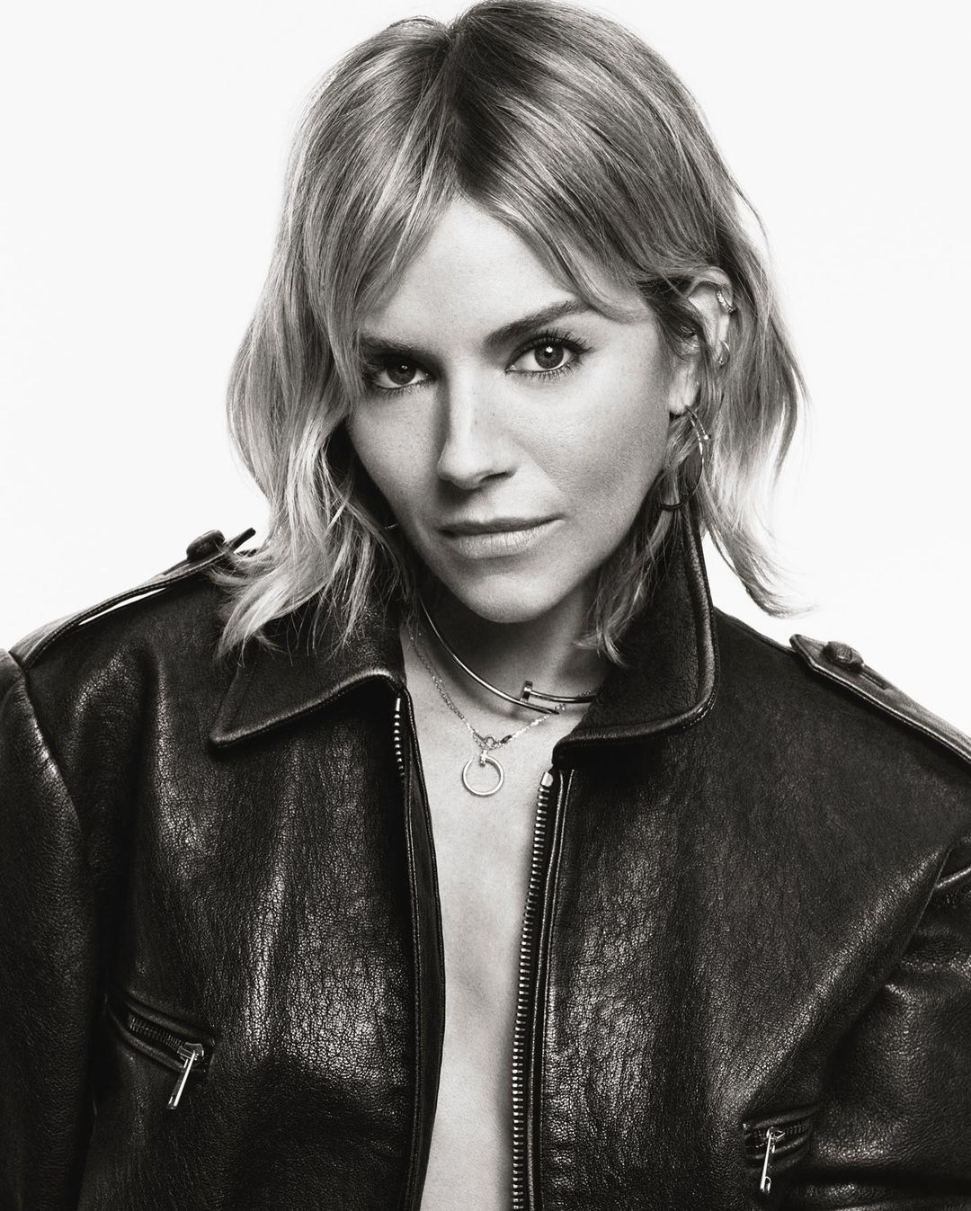 Portrait of actress Sienna Miller wearing a black leather jacket against a seamless white background, photographed by Tom Schirmacher.