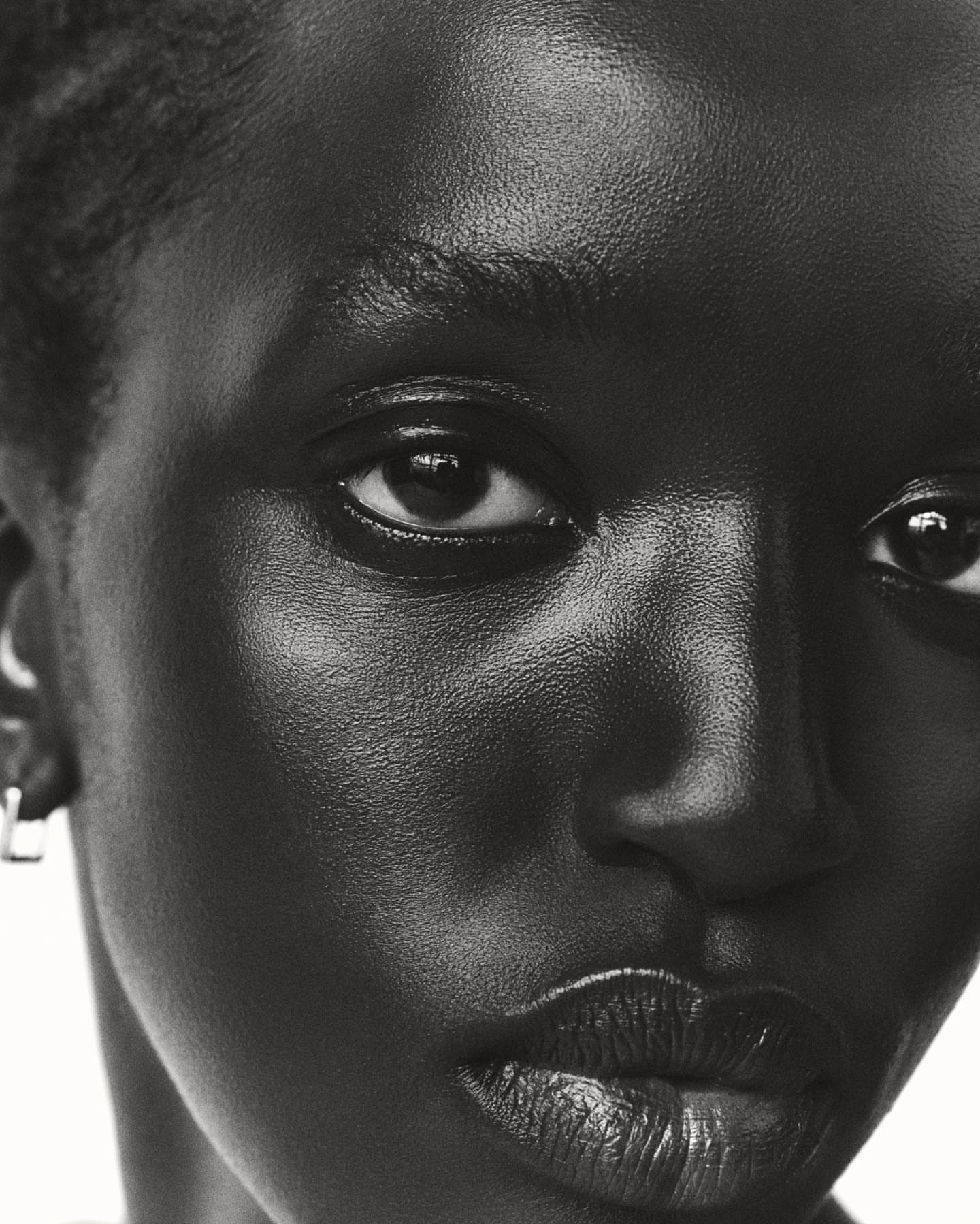 Close-up black and white portrait of a black woman wearing small silver hoop earrings against a bright white background.