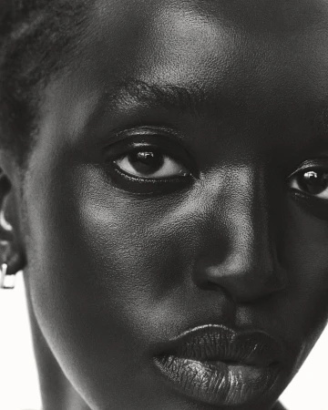 Close-up black and white portrait of a black woman wearing small silver hoop earrings against a bright white background.