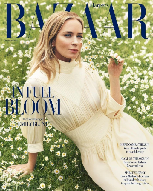 Emily Blunt on Harper's Bazaar cover, wearing a cream dress and holding small white flowers in a field of daisies.