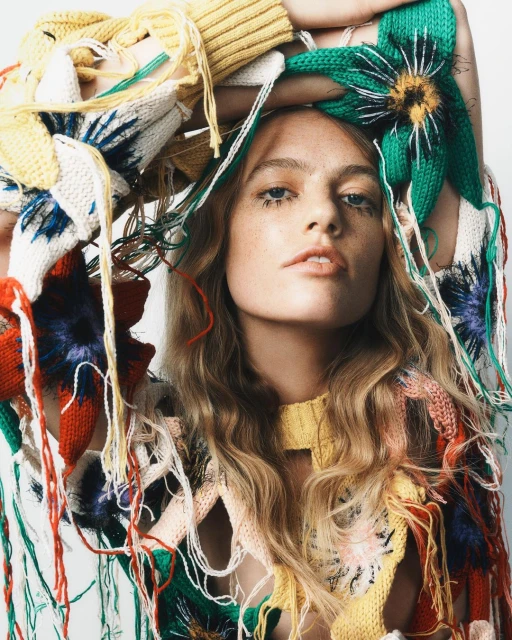 Fashionable portrait of a model wearing a colorful, floral-patterned knit top with loose strands, set against a plain, bright background.