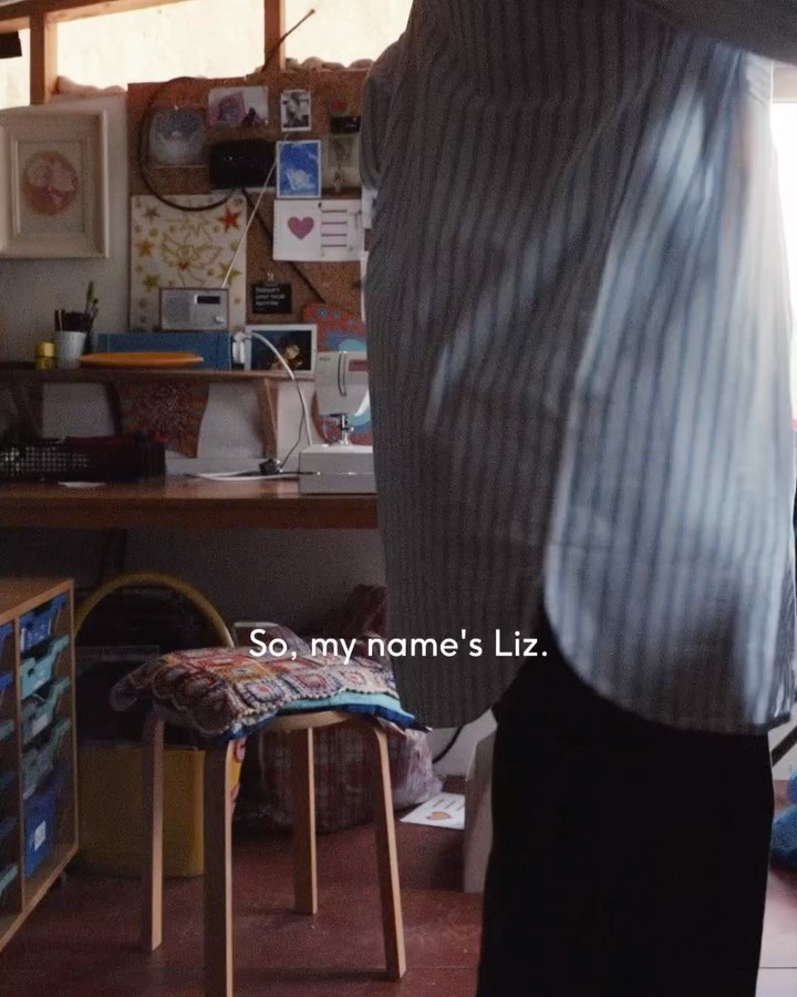 Person in a striped shirt standing in a brightly lit, cluttered crafting room with a sewing machine and various supplies on a table.