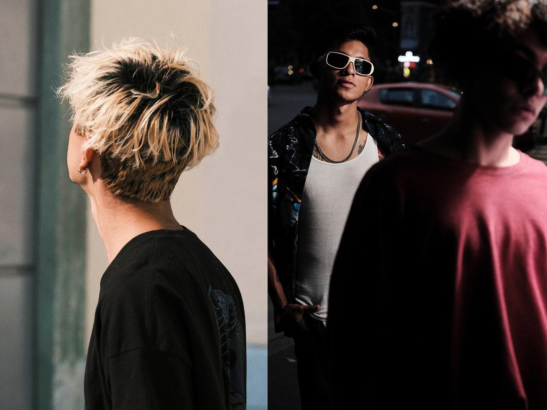Eye-level shot of three young adult males in casual street fashion, standing outdoors with a blurred street and vehicle in the background.