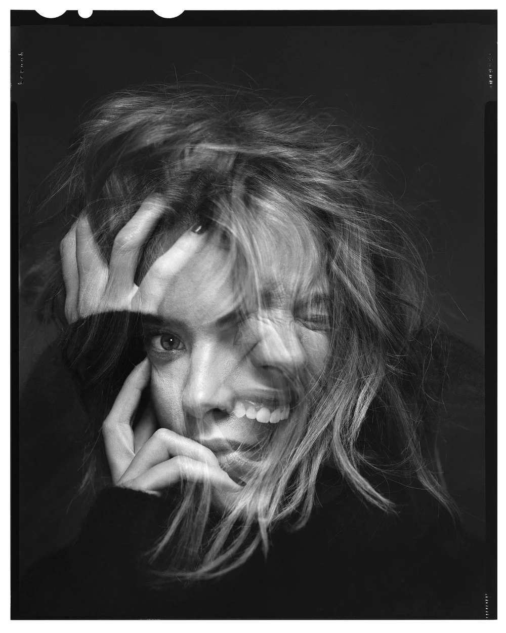 Monochrome portrait of a woman with multiple exposure effect, layered facial expressions, and a hand touching her face in a dark setting.