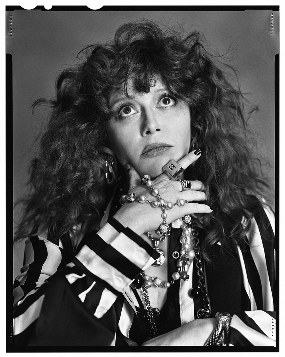 Portrait of a woman with curly hair wearing striped shirt and jewelry in a photo studio setting with soft, even lighting.