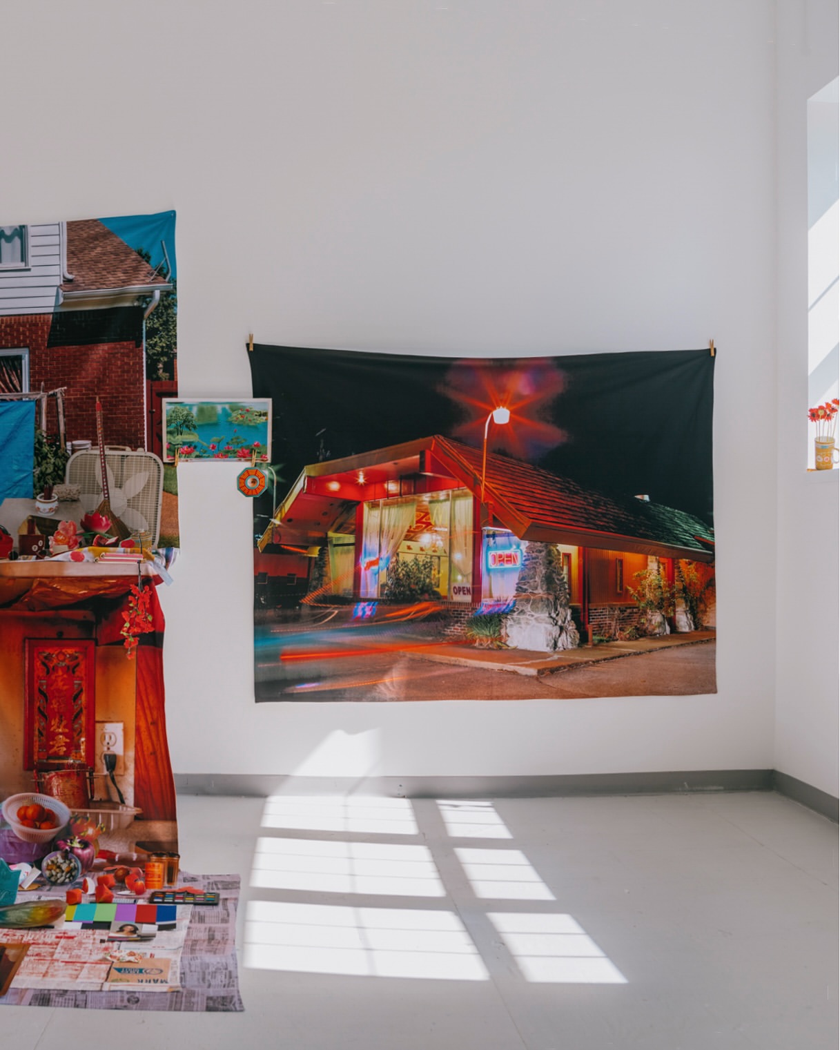 Interior view of a white room with photographic art pieces hanging on the walls and light creating shadow patterns on the floor.