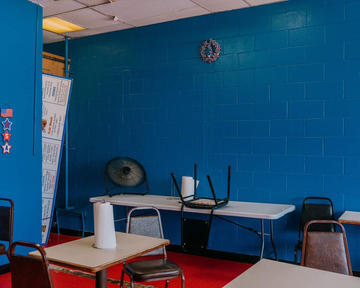 Interior of a brightly colored diner features blue walls, white folding tables with brown chairs, and American themed decor.