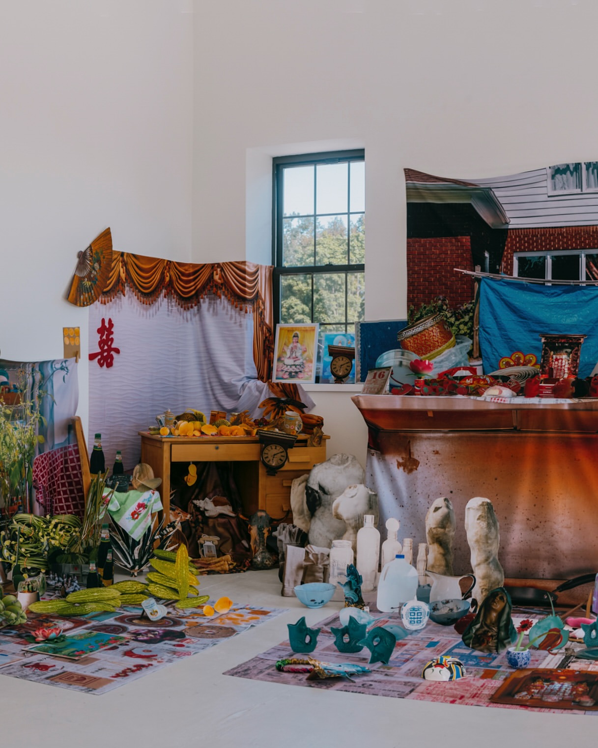 Photo studio scene with assorted objects including household items, plants, and sculptures arranged on rugs and tables against white walls.