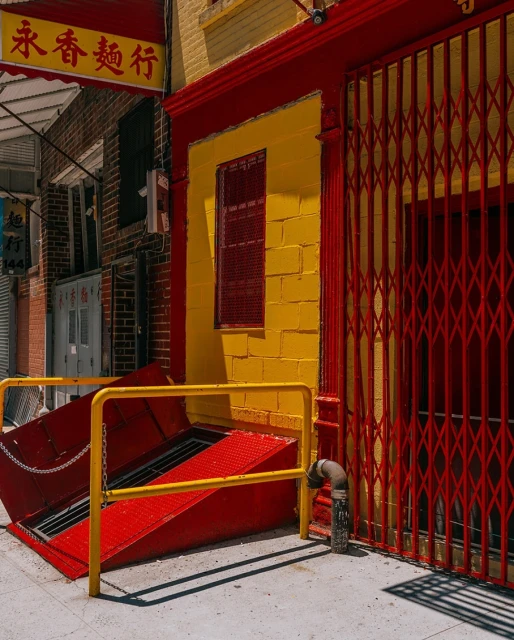 Vibrant yellow and red building exterior with an open cellar door and metal security gate in an urban setting, showcasing bold colors.