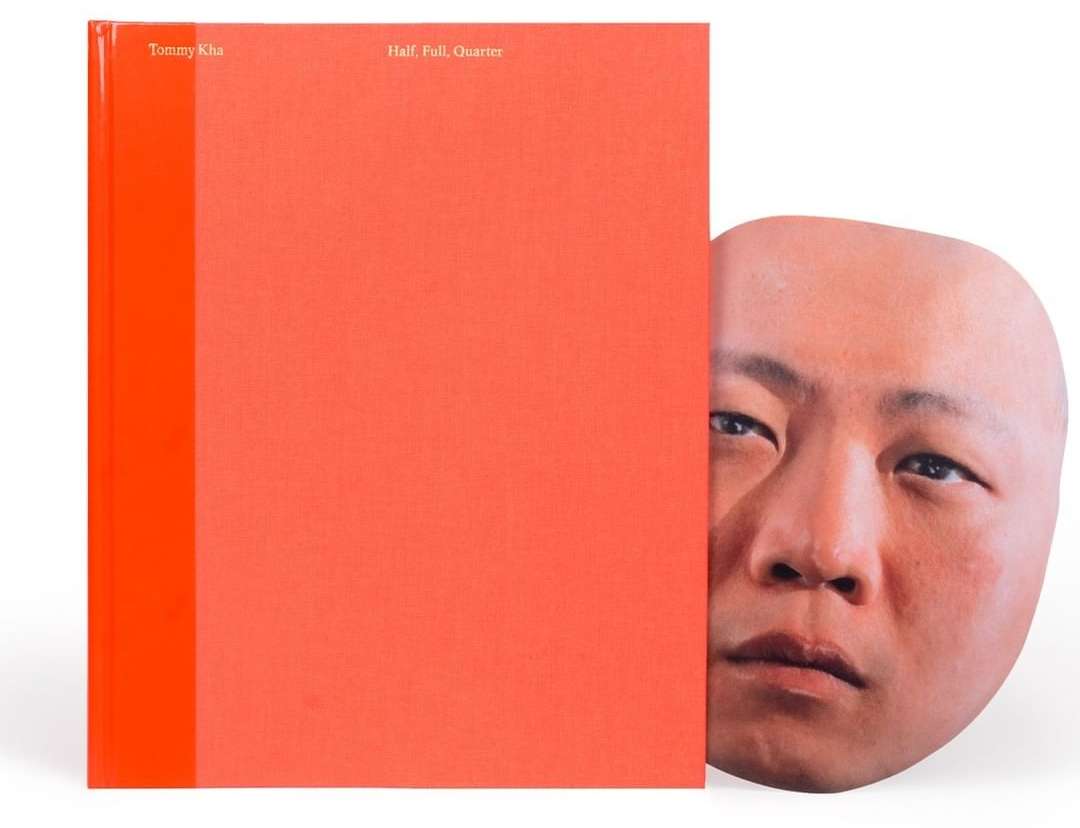 Book cover with title 'Half, Full, Quarter' by Tommy Kha next to a lifelike mask of a bald Asian man's face on a white background.