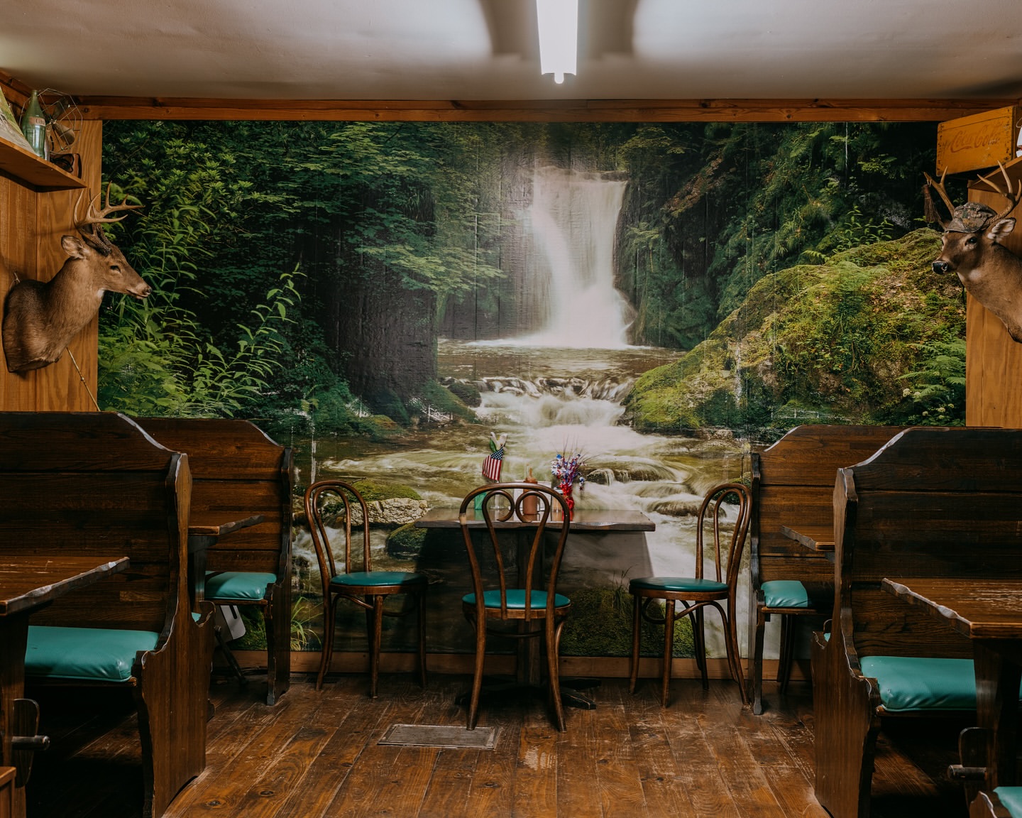Restaurant interior with wooden booths, waterfall mural, and deer mounts, creating a rustic, nature-themed dining atmosphere.