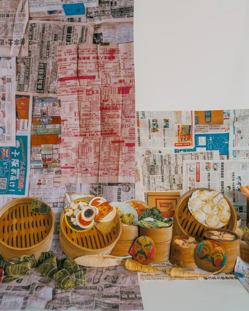 Overhead shot of bamboo steamer baskets filled with dim sum against a background of newspaper clippings and a blank white canvas.