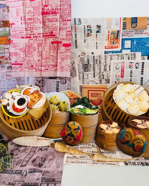 Artful food still life of varied Asian dumplings and dim sum in bamboo steamers against a backdrop of vintage newspaper clippings.