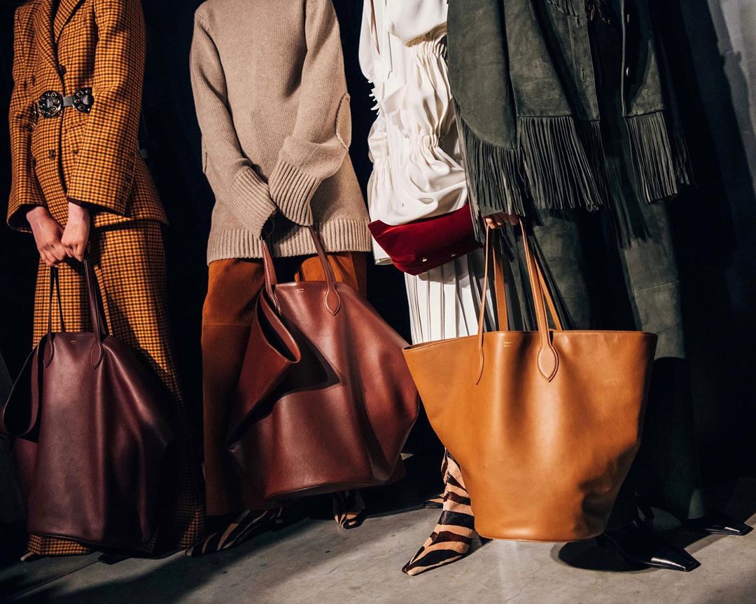 Three models display tan and burgundy leather tote bags, showcasing modern fashion and style in a studio setting with neutral clothing.