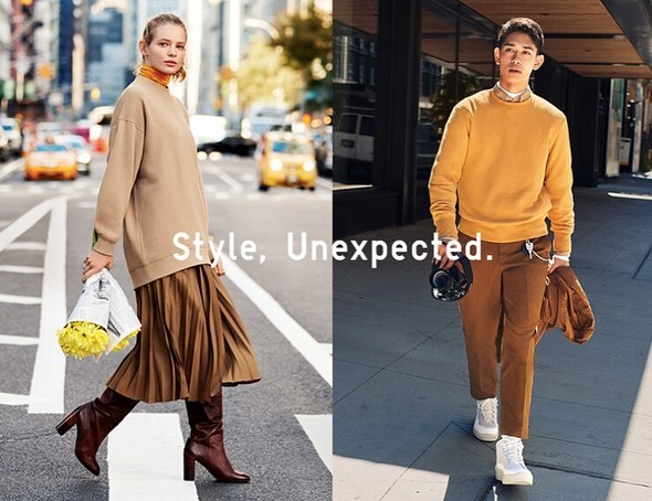 A woman crosses an urban street wearing a sweater, skirt, and boots, while a man in a sweater and trousers walks along the sidewalk.