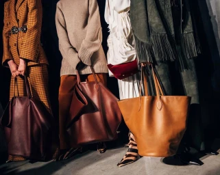 Four models holding large leather tote bags while wearing coats, trousers, and patterned boots.