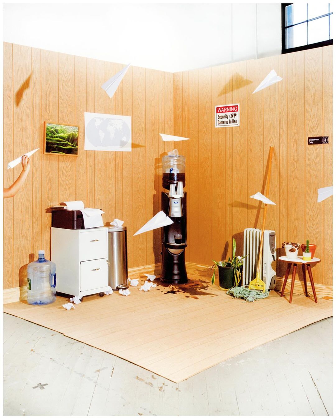 Office break room with flying paper airplanes, spilled coffee, and a water cooler; a humorous and chaotic office still life scene.