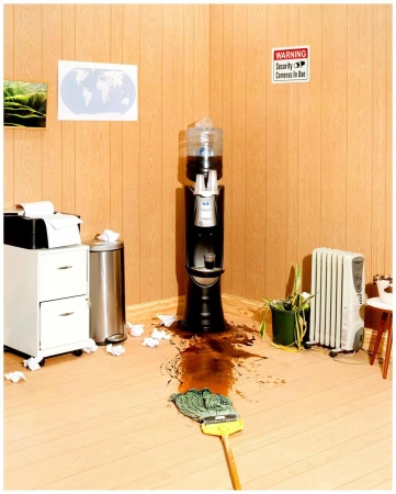 Office spill with mop next to spilled liquid and a water cooler. Cabinet, trash can, heater, and warning sign are also present.