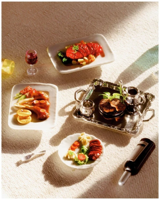 Overhead shot of miniature food dishes on a textured white surface featuring small portions of meat, salad, and drinks.