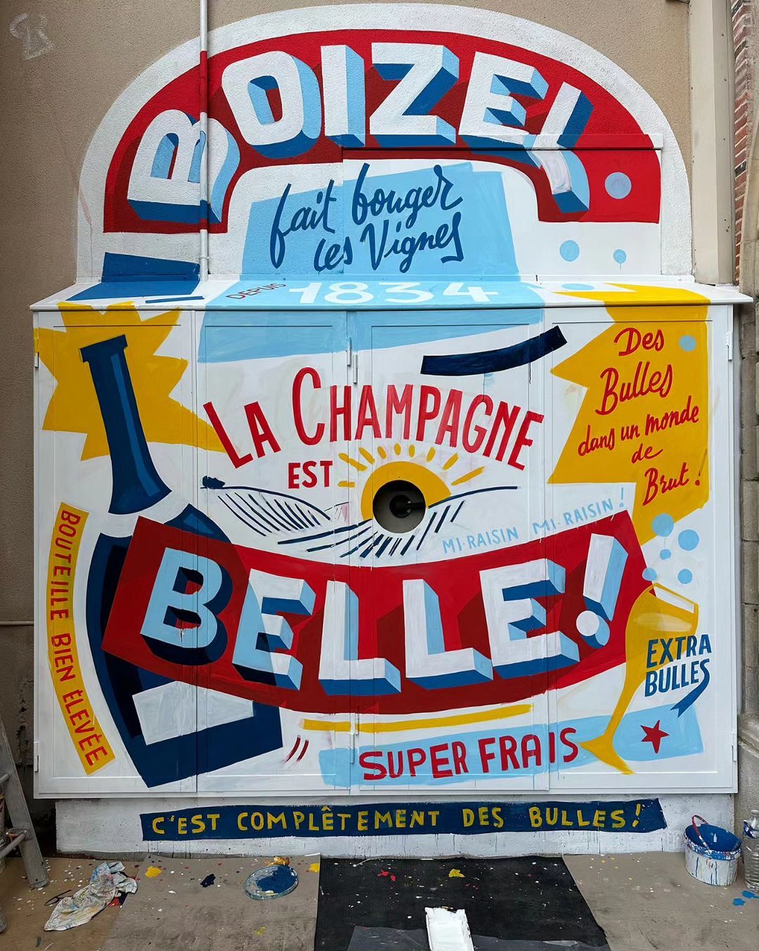 Painted advertisement on a white wooden surface featuring typography for champagne, with a vintage aesthetic and red, white, and blue colors.