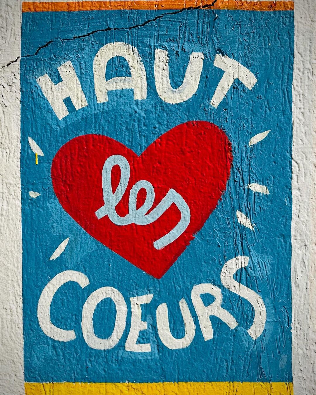 A painted mural on a wall with a blue background and a large red heart featuring white lettering that says, 'Haut Les Coeurs'.