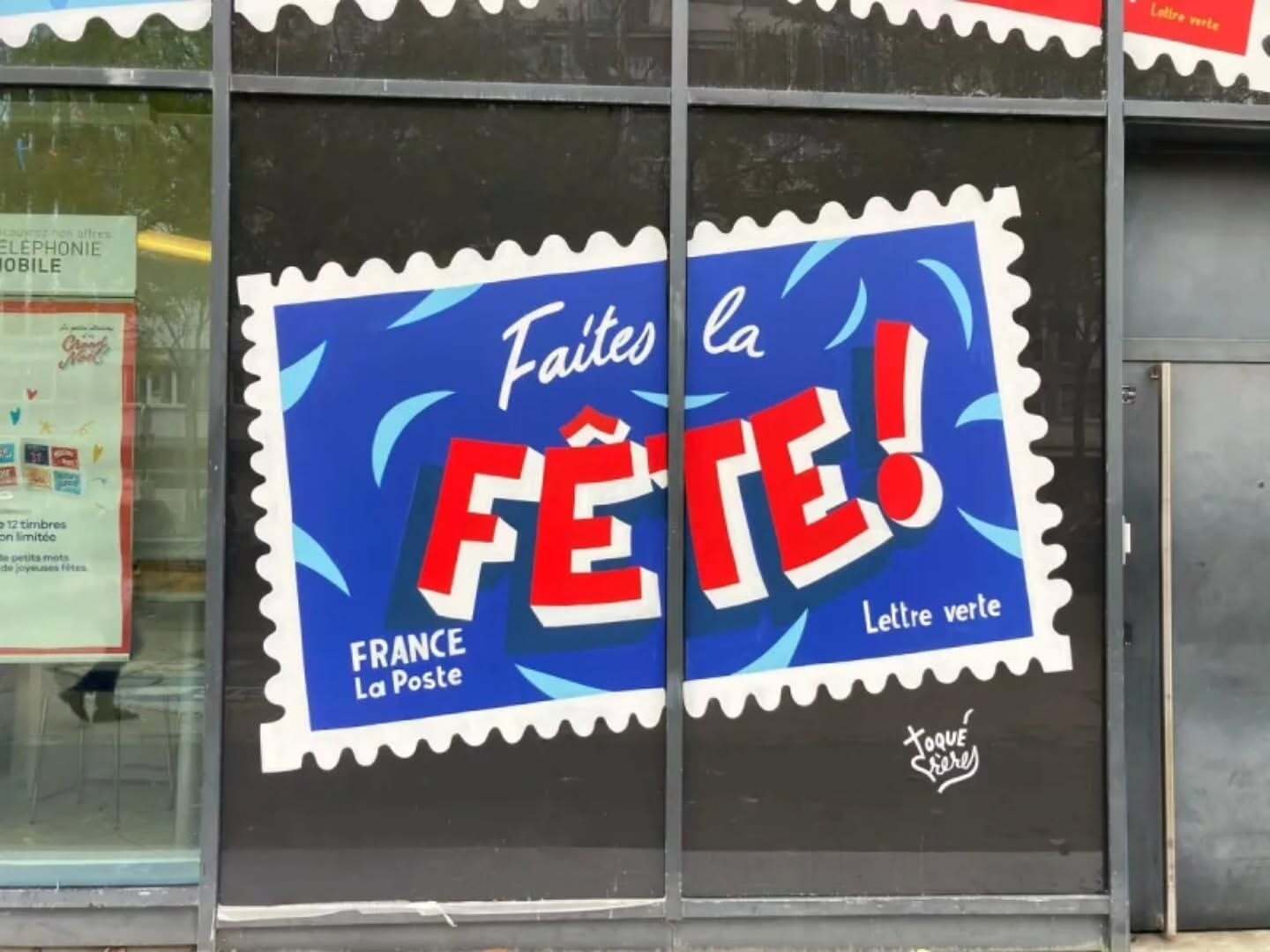 A large poster on a building window advertises 'Faites la Fête!' in red and white text against a blue background, resembling a stamp.
