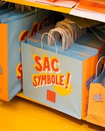 Close-up of stacked light blue and orange paper shopping bags with bold red lettering on a shelf.