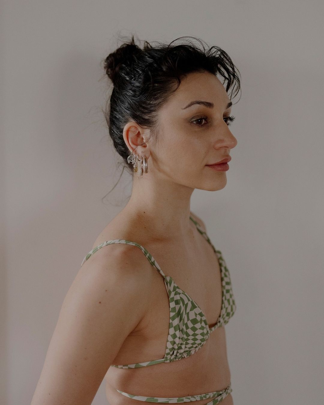 Woman in checkered bikini top, side profile with silver earrings against a plain background. Studio lighting with a shallow depth of field.