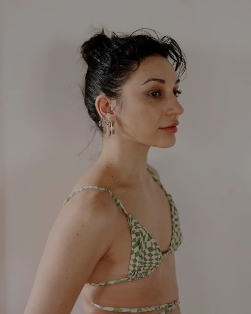 Woman in checkered bikini top, side profile with silver earrings against a plain background. Studio lighting with a shallow depth of field.
