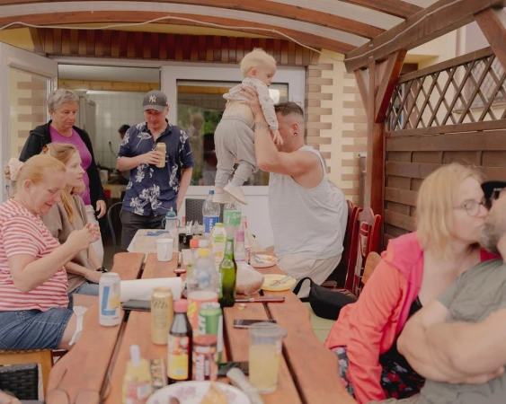Outdoor gathering with family and friends, featuring an adult male holding up a young child in a backyard setting.